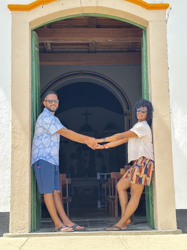 Marcele e Samuel de mãos dadas em frente a uma capela